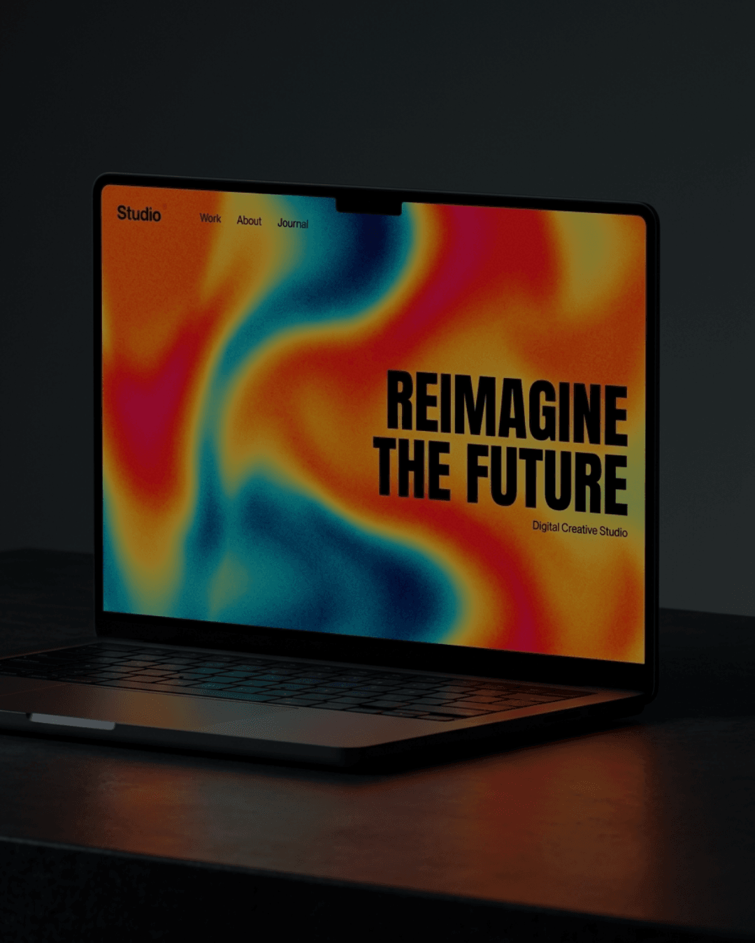 A laptop open on a dark desk, its screen filled with a vivid orange and blue gradient behind bold black display type, the glow reflecting across the surface
